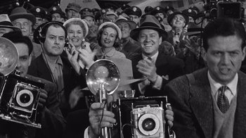 Movie still from “It Should Happen to You” (1954), directed by George Cukor – A group of men and women holding a camera in front of a crowd of onlookers; Medium shot, Low angle