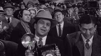 Movie still from “It Should Happen to You” (1954), directed by George Cukor – A group of men in suits and hats are standing in a crowd; Medium shot, Low angle