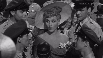 Movie still from “It Should Happen to You” (1954), directed by George Cukor – An old photo of a woman surrounded by a group of men; Close Up shot, High angle
