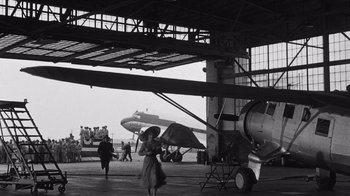 Movie still from “It Should Happen to You” (1954), directed by George Cukor – A woman holding an umbrella in front of an airplane; Extreme Wide shot, Low angle