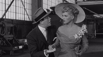 Movie still from “It Should Happen to You” (1954), directed by George Cukor – A man and a woman wearing hats and holding hands in an industrial setting; Medium shot, Over the shoulder angle