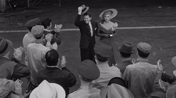 Movie still from “It Should Happen to You” (1954), directed by George Cukor – A man and a woman standing next to each other in front of a crowd; Wide shot, High angle