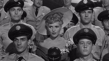 Movie still from “It Should Happen to You” (1954), directed by George Cukor – A group of men in uniform with a woman in a hat; Close Up shot, Low angle