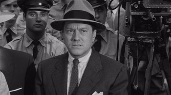 Movie still from “It Should Happen to You” (1954), directed by George Cukor – A man in a suit and a hat is in front of a group of men; Close Up shot, Over the shoulder angle