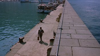 Movie still from “It Started in Naples” (1960), directed by Melville Shavelson – A man in a suit and tie walking down a pier; Extreme Wide shot, High angle