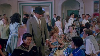 Movie still from “It Started in Naples” (1960), directed by Melville Shavelson – A man in a suit and hat standing in front of a group of people; Wide shot, High angle