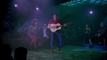 Movie still from “It Started in Naples” (1960), directed by Melville Shavelson – A man playing a guitar in front of a group of people; Wide shot, Low angle