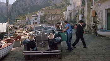 Movie still from “It Started in Naples” (1960), directed by Melville Shavelson – Two men walking past an old car on a street; Wide shot, High angle