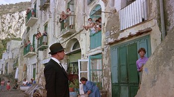 Movie still from “It Started in Naples” (1960), directed by Melville Shavelson – A man wearing a suit and hat standing in front of a building; Wide shot, Low angle