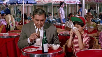 Movie still from “It Started in Naples” (1960), directed by Melville Shavelson – An older man sitting at a table with a bottle of wine; Medium shot, High angle