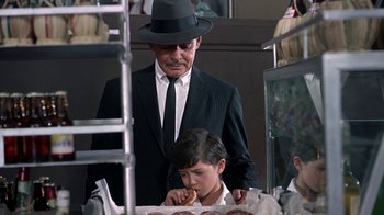 Movie still from “It Started in Naples” (1960), directed by Melville Shavelson – A man in a suit and a hat eating a sandwich; Medium shot, Over the shoulder angle