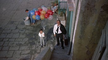 Movie still from “It Started in Naples” (1960), directed by Melville Shavelson – A man and a boy standing on steps with balloons in the background; Wide shot, High angle