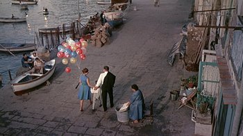 Movie still from “It Started in Naples” (1960), directed by Melville Shavelson – A group of people standing on a sidewalk next to a body of water; Wide shot, High angle