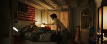 Movie still from “It Takes Three” (2021), directed by Scott Coffey – A woman standing on top of a bed holding a remote; Wide shot, Low angle