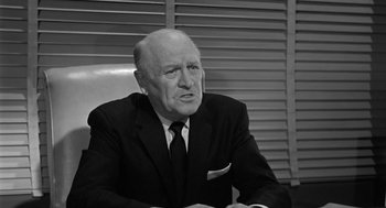 Movie still from “It! The Terror from Beyond Space” (1958), directed by Edward L. Cahn – An older man wearing a suit and tie sitting at a desk; Close Up shot, Low angle