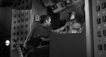 Movie still from “It! The Terror from Beyond Space” (1958), directed by Edward L. Cahn – A black and white photo of a man working on a computer; Medium shot, Low angle