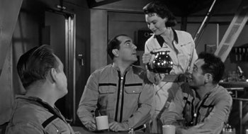 Movie still from “It! The Terror from Beyond Space” (1958), directed by Edward L. Cahn – A man and a woman are talking to another man in front of a table; Medium shot, Over the shoulder angle