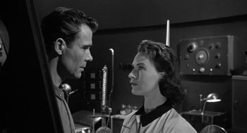 Movie still from “It! The Terror from Beyond Space” (1958), directed by Edward L. Cahn – A man and a woman standing next to each other in a room; Close Up shot, Over the shoulder angle