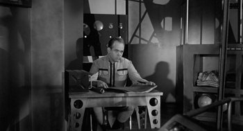 Movie still from “It! The Terror from Beyond Space” (1958), directed by Edward L. Cahn – A man sitting at a table in a room; Medium shot, Low angle