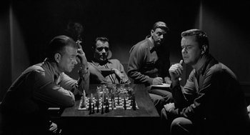 Movie still from “It! The Terror from Beyond Space” (1958), directed by Edward L. Cahn – A group of men sitting at a table playing a game of chess; Medium shot, High angle
