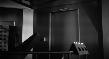 Movie still from “It! The Terror from Beyond Space” (1958), directed by Edward L. Cahn – A black and white photo of a door to a building; Medium shot, Low angle