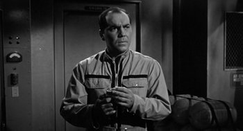 Movie still from “It! The Terror from Beyond Space” (1958), directed by Edward L. Cahn – A man holding a cell phone while standing in front of a door; Medium shot, Low angle