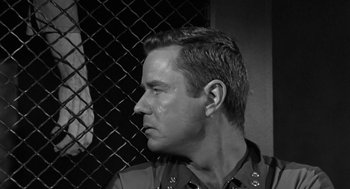 Movie still from “It! The Terror from Beyond Space” (1958), directed by Edward L. Cahn – Black and white photograph of a man in a police uniform; Close Up shot, Over the shoulder angle