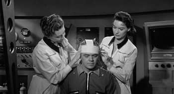 Movie still from “It! The Terror from Beyond Space” (1958), directed by Edward L. Cahn – A man being fitted for a plastic surgery procedure by two nurses; Medium shot, Low angle