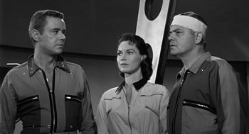 Movie still from “It! The Terror from Beyond Space” (1958), directed by Edward L. Cahn – A black - and - white photo of a woman and two men; Medium shot, Low angle