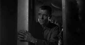 Movie still from “It! The Terror from Beyond Space” (1958), directed by Edward L. Cahn – Black and white photograph of a man looking out of a window; Close Up shot, Low angle