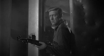Movie still from “It! The Terror from Beyond Space” (1958), directed by Edward L. Cahn – A black and white photo of a man holding a gun; Medium shot, Low angle