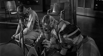 Movie still from “It! The Terror from Beyond Space” (1958), directed by Edward L. Cahn – A man with a gas mask is sitting in a chair; Medium shot, High angle