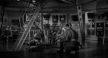 Movie still from “It! The Terror from Beyond Space” (1958), directed by Edward L. Cahn – A black and white photo of a group of people in a room; Wide shot, Low angle