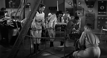 Movie still from “It! The Terror from Beyond Space” (1958), directed by Edward L. Cahn – A black and white photo of people working in an industrial setting; Wide shot, Low angle