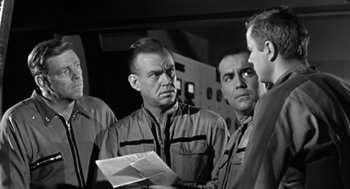 Movie still from “It! The Terror from Beyond Space” (1958), directed by Edward L. Cahn – A group of men standing next to each other in a room; Medium shot, Over the shoulder angle