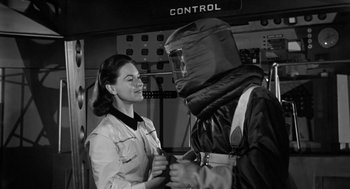 Movie still from “It! The Terror from Beyond Space” (1958), directed by Edward L. Cahn – A woman and a man wearing a suit and a gas mask; Medium shot, Low angle