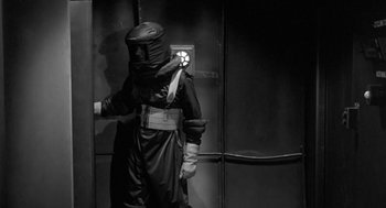 Movie still from “It! The Terror from Beyond Space” (1958), directed by Edward L. Cahn – A person in a costume standing next to a wall; Medium shot, Low angle