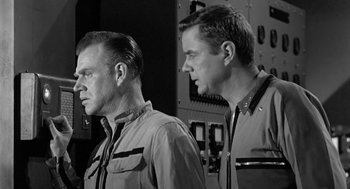 Movie still from “It! The Terror from Beyond Space” (1958), directed by Edward L. Cahn – A black - and - white photo of two men standing next to each other; Medium shot, Low angle