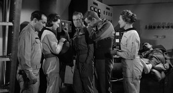 Movie still from “It! The Terror from Beyond Space” (1958), directed by Edward L. Cahn – A black and white photo of a group of people; Medium shot, Low angle