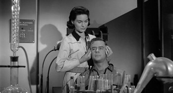 Movie still from “It! The Terror from Beyond Space” (1958), directed by Edward L. Cahn – A woman standing next to a man in front of a mirror; Medium shot, Low angle