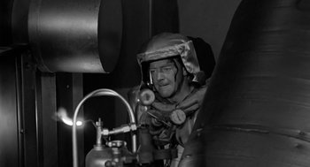 Movie still from “It! The Terror from Beyond Space” (1958), directed by Edward L. Cahn – A man wearing a gas mask in a confined space; Medium shot, High angle