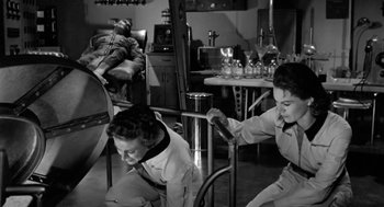 Movie still from “It! The Terror from Beyond Space” (1958), directed by Edward L. Cahn – A black and white photo of people working in a room; Wide shot, High angle