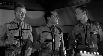 Movie still from “It! The Terror from Beyond Space” (1958), directed by Edward L. Cahn – A group of men standing next to each other holding a cell phone; Medium shot, Over the shoulder angle