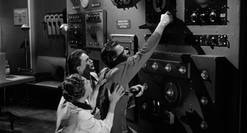 Movie still from “It! The Terror from Beyond Space” (1958), directed by Edward L. Cahn – A group of people standing next to each other in a room; Medium shot, High angle