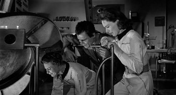 Movie still from “It! The Terror from Beyond Space” (1958), directed by Edward L. Cahn – A group of men and women working on a project; Medium shot, Low angle