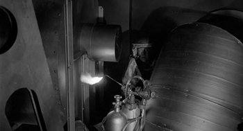 Movie still from “It! The Terror from Beyond Space” (1958), directed by Edward L. Cahn – A black - and - white photo of a man working in an industrial setting; Medium shot, Low angle