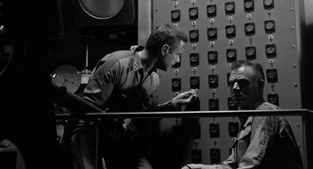 Movie still from “It! The Terror from Beyond Space” (1958), directed by Edward L. Cahn – A black and white photo of a man looking down at his phone; Medium shot, Low angle