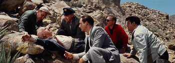 Movie still from “It's a Mad Mad Mad Mad World” (1963), directed by Stanley Kramer – A group of men sitting next to each other on some rocks; Medium shot, High angle