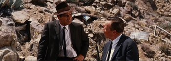 Movie still from “It's a Mad Mad Mad Mad World” (1963), directed by Stanley Kramer – A man in a suit and a hat talking to another man in a suit and a hat; Medium shot, Over the shoulder angle