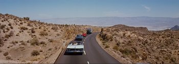 Movie still from “It's a Mad Mad Mad Mad World” (1963), directed by Stanley Kramer – A group of cars driving down a road next to a hill; Extreme Wide shot, High angle